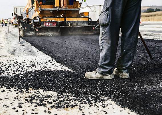 Worker operating asphalt paver machine during road construction and repairing works